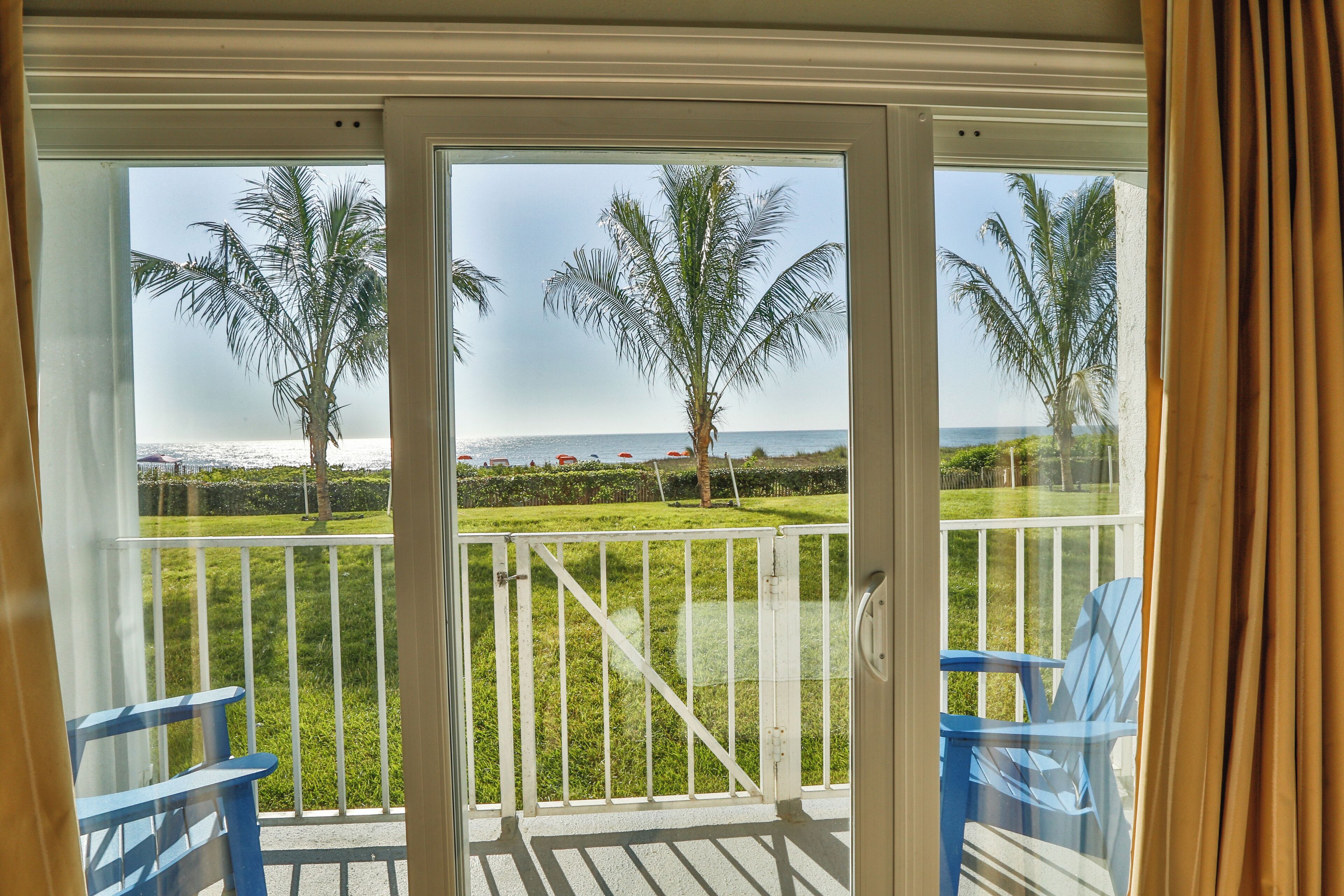 A balcony with a view of the sea, palm trees, and a grassy area.