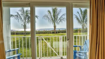 A balcony with a view of the sea, palm trees, and a grassy area.