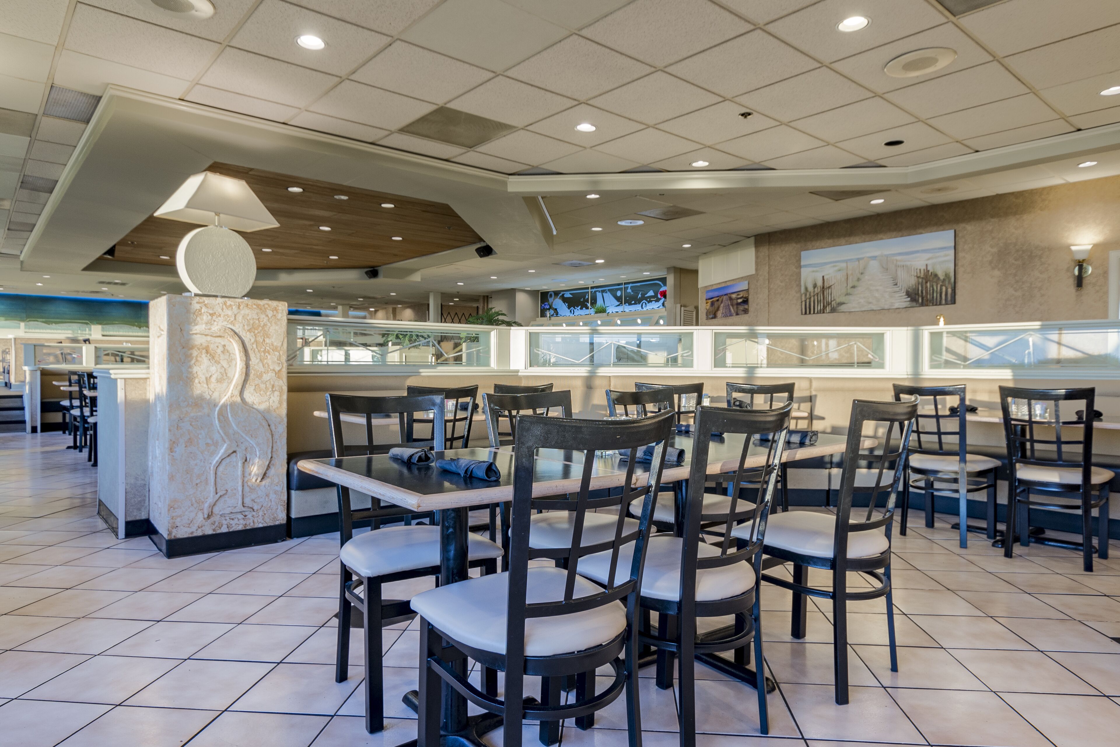 A spacious restaurant with multiple dining tables and chairs, a central decorative pillar, and a modern ceiling design.