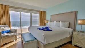 A hotel room with a large bed, a bench, a nightstand, and a view of the ocean.