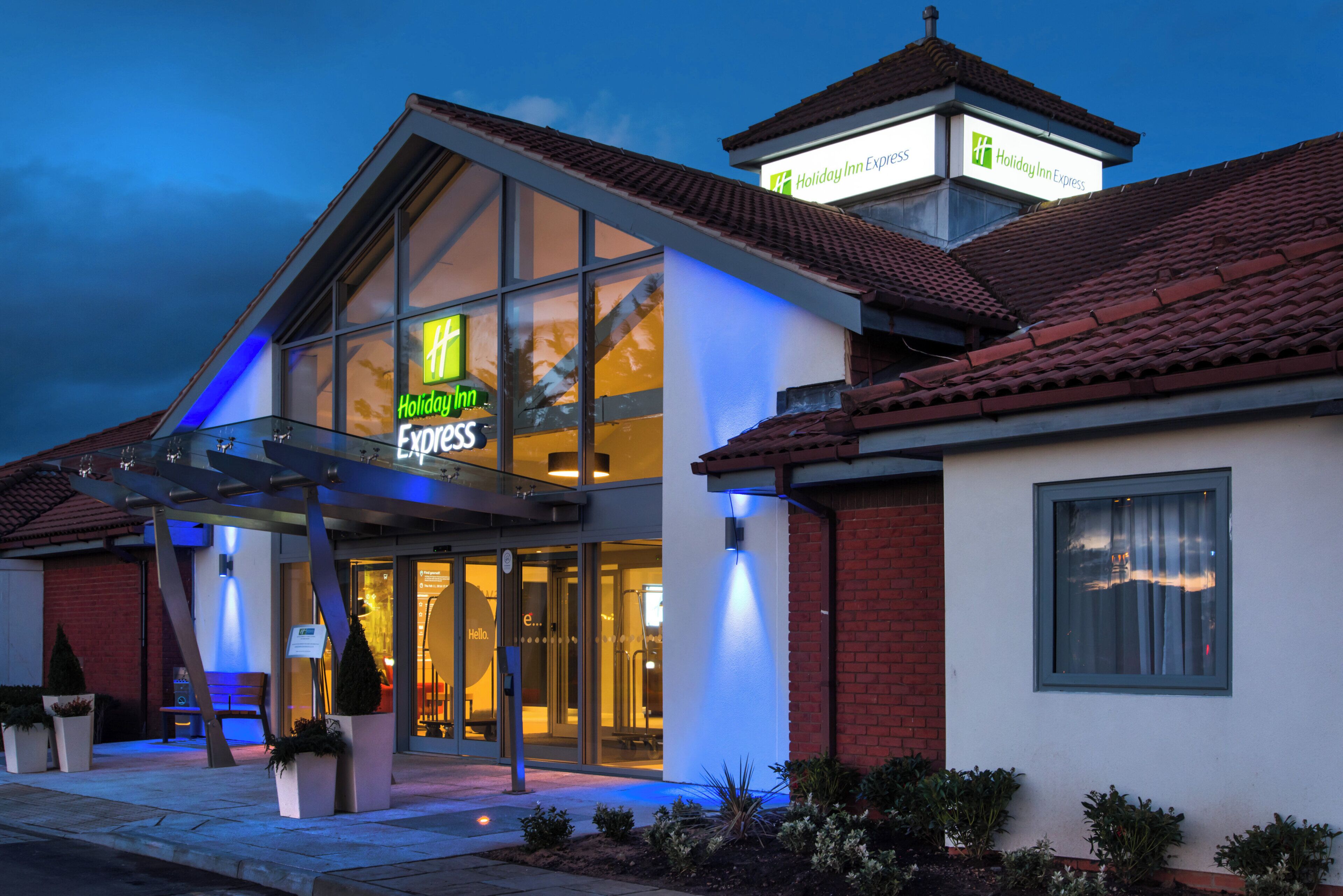 Un bâtiment de l’hôtel Holiday Inn Express avec une entrée en verre, un toit recouvert de tuiles rouges et une enseigne au-dessus de l’entrée.