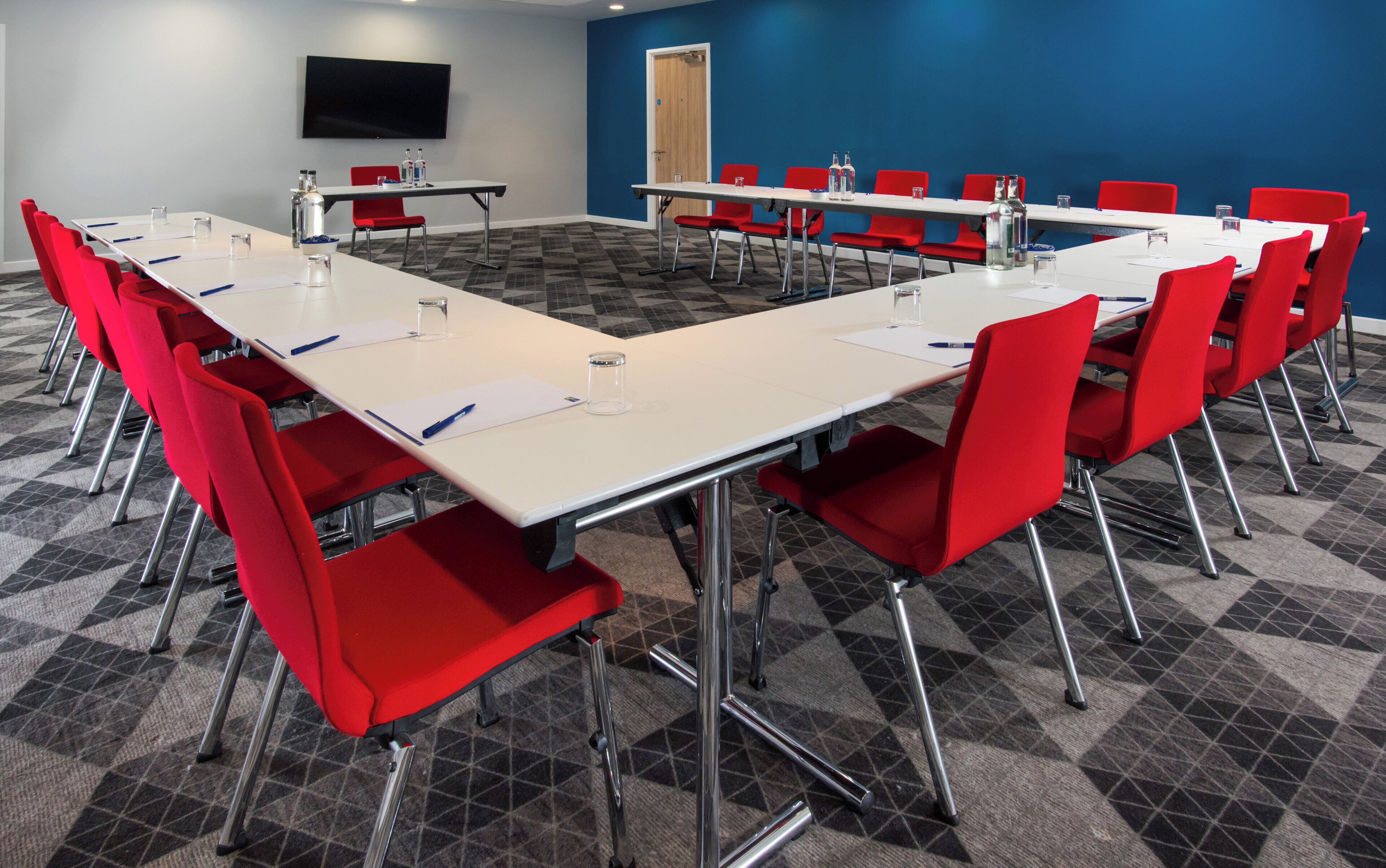 A conference room with a large table, red chairs, and a flat-screen TV on the wall.