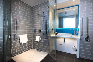 Un baño moderno con ducha de vidrio, un lavabo blanco y una pared de acento azul.