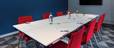 Un salón de conferencias con una larga mesa, sillas rojas y un televisor de pantalla plana en la pared.