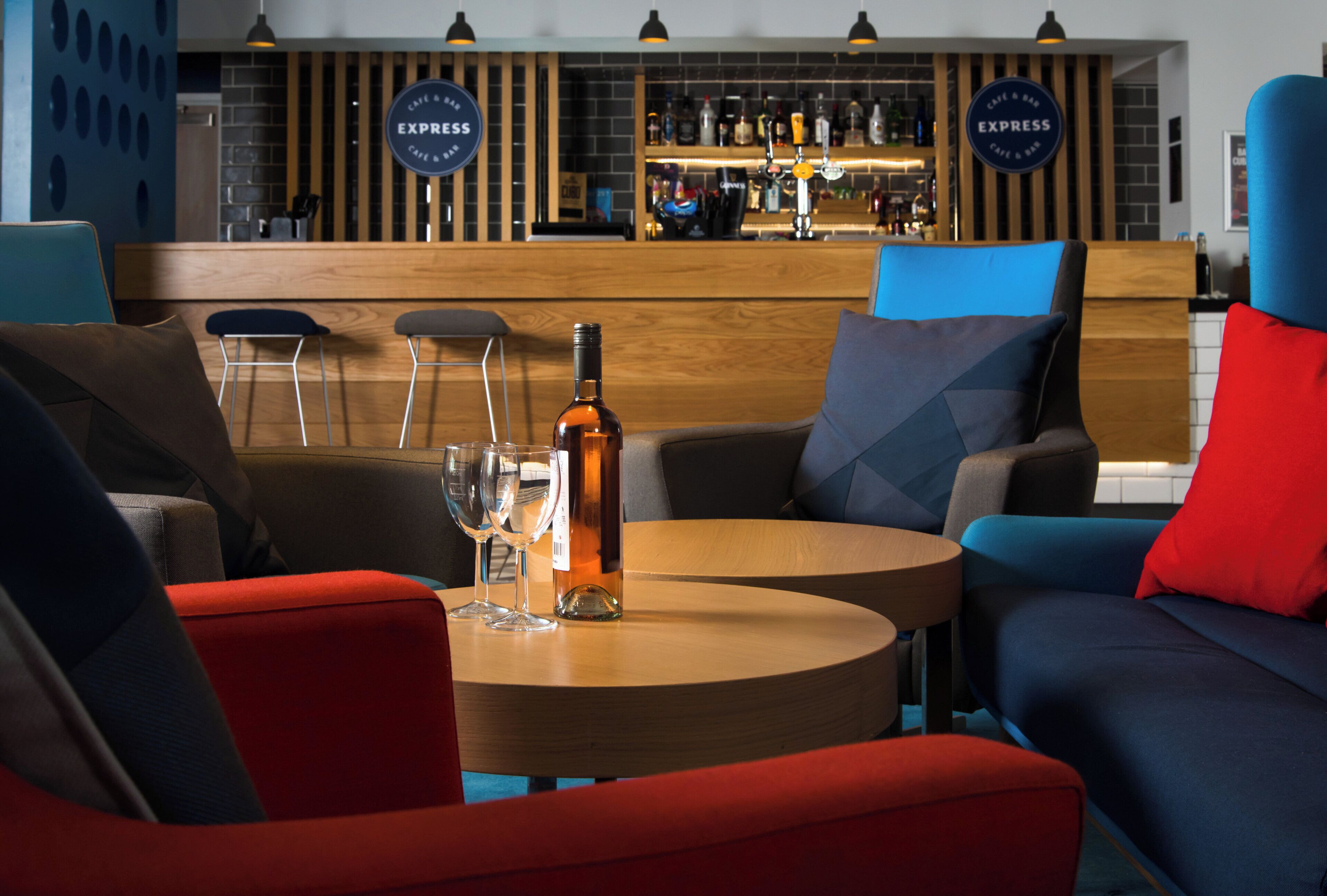 A bar area with two round tables, bar stools, and a bottle of wine on one table.