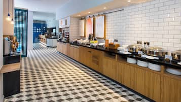 A modern breakfast bar with a geometric patterned floor, a counter with food and drink dispensers, and a wall with informational signs.