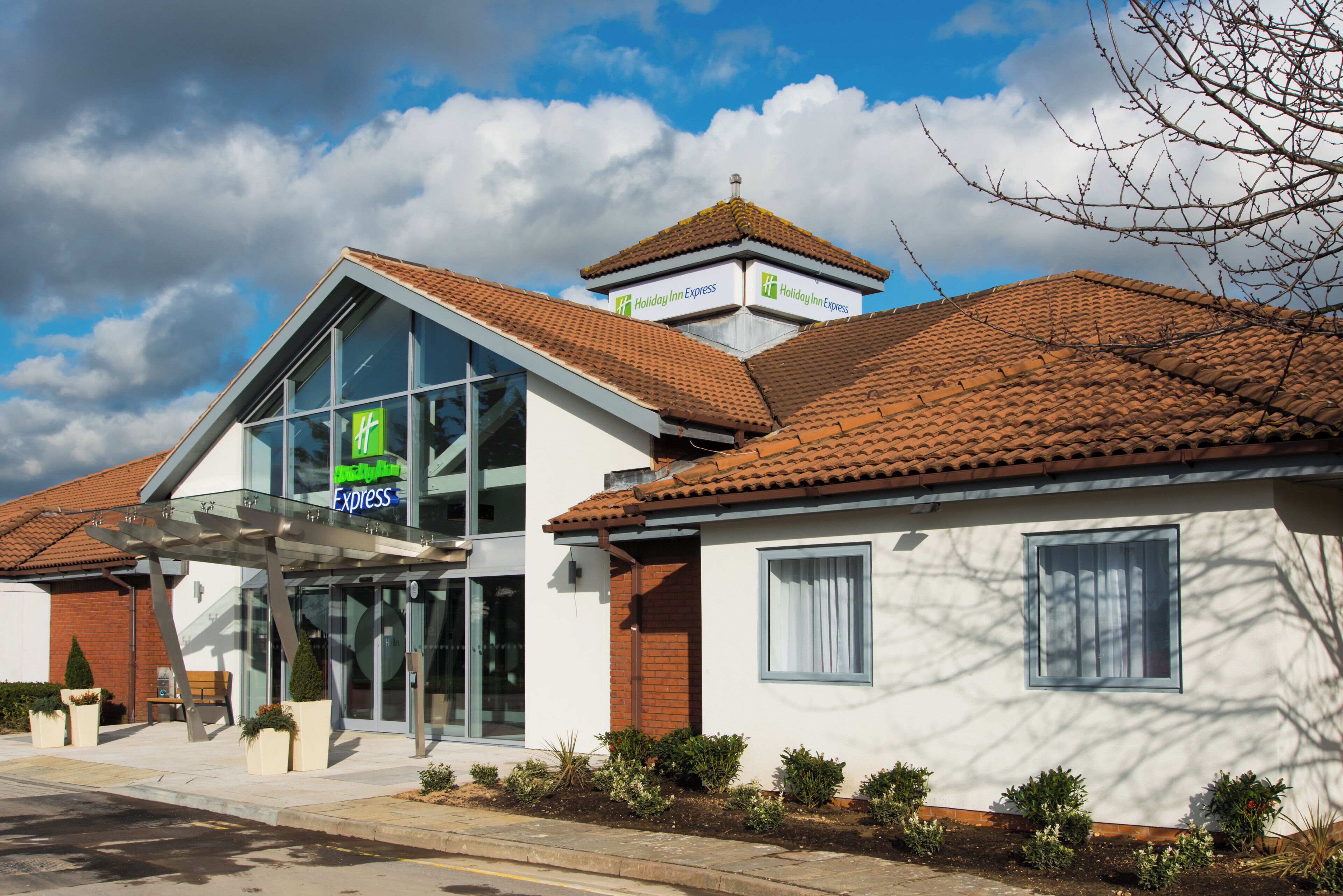 A Holiday Inn Express building with a modern glass entrance, a traditional tiled roof, and a clear sky.