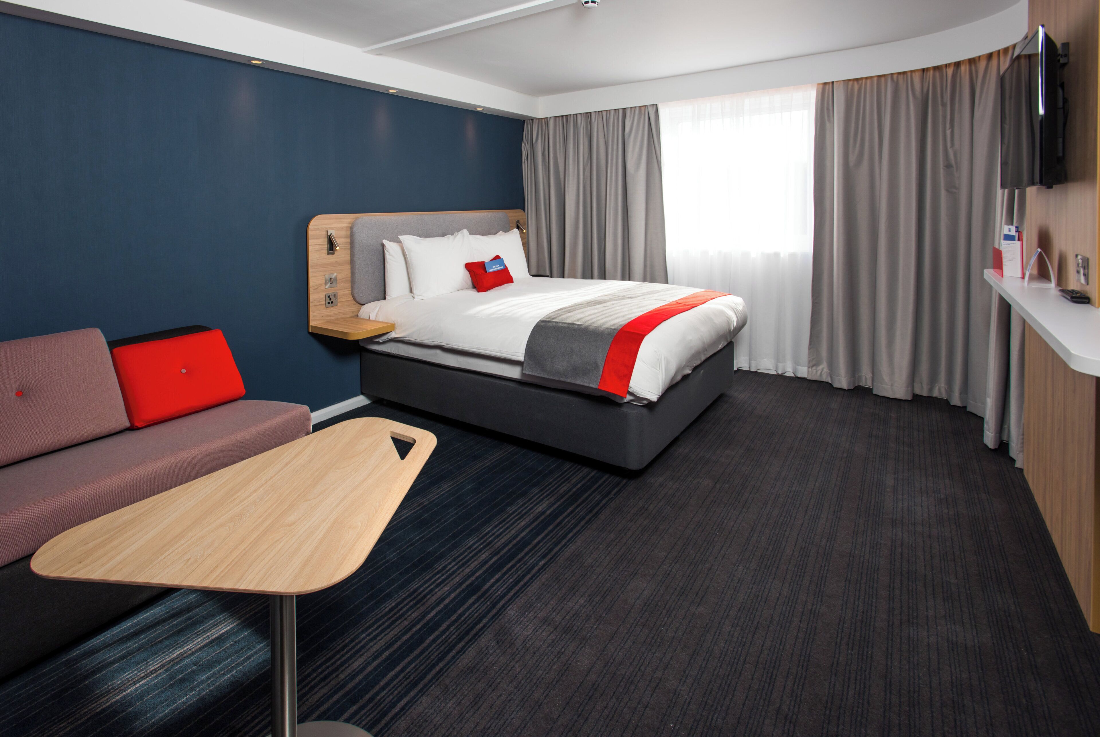 A hotel room with a bed, a sofa, a small table, and a TV.
