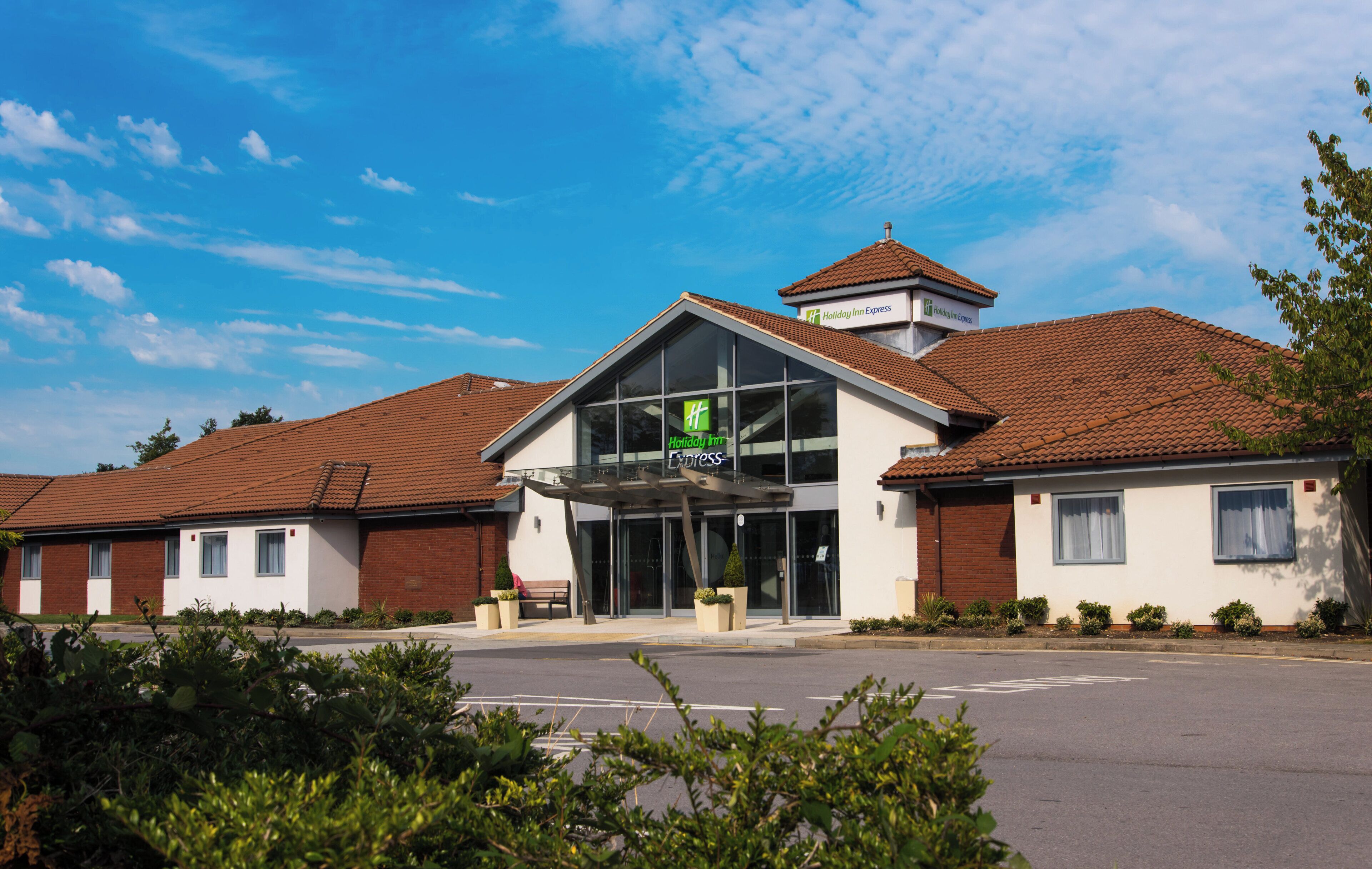 A Holiday Inn Express hotel with a modern design, featuring a prominent entrance, a covered patio area, and a parking lot in front.