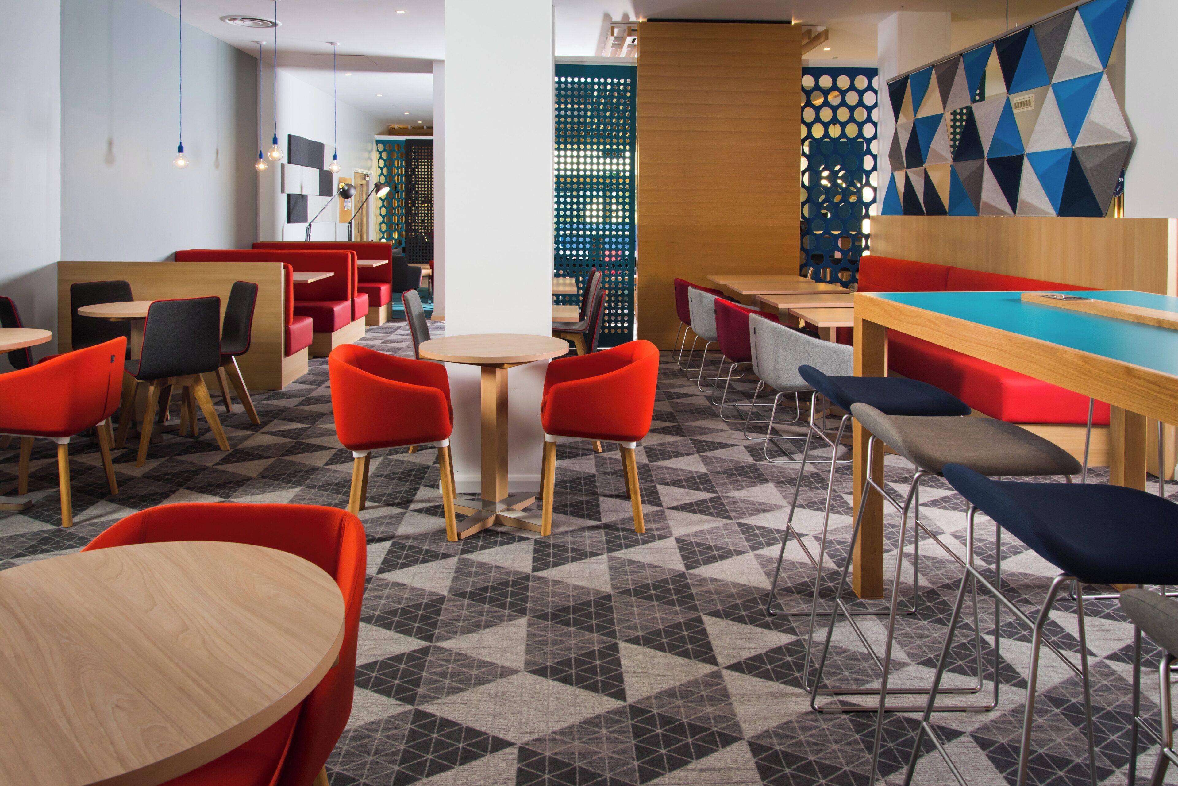 Ein modernes Restaurant mit roten und grauen Stühlen, Holztischen und einem geometrisch gemusterten Boden.