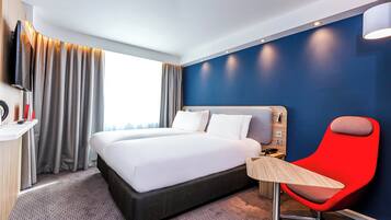 A hotel room with a large bed, a desk with a chair, a TV, and a window with curtains.