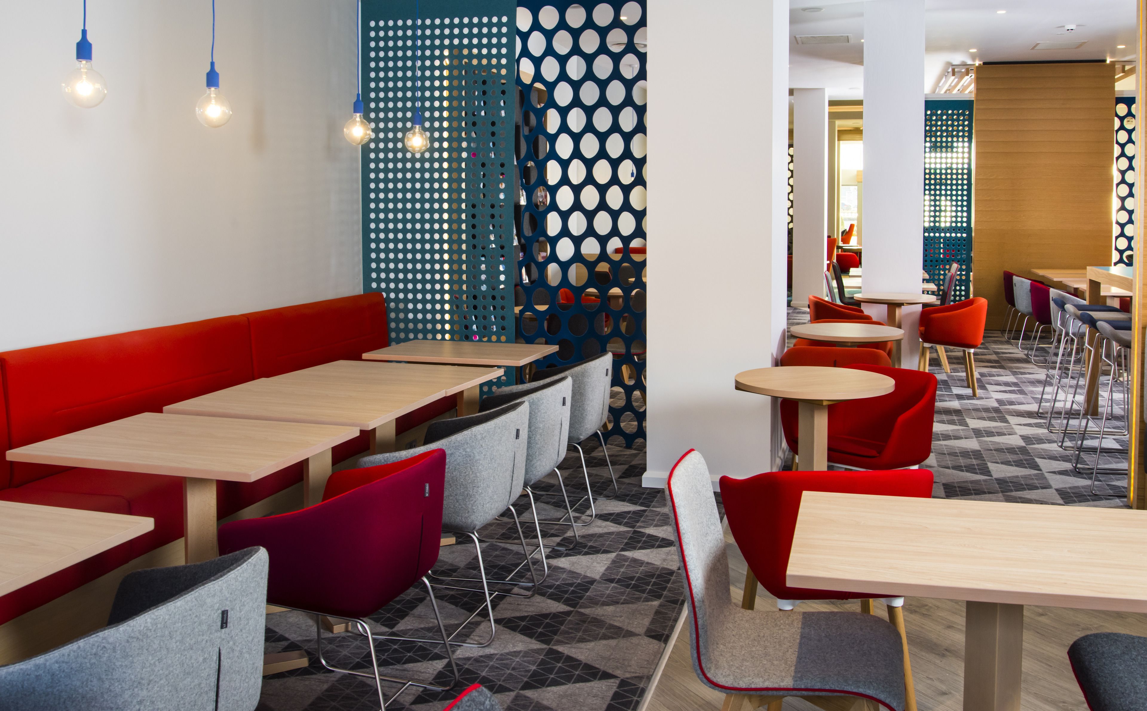 A modern restaurant with red and grey seating, wooden tables, and a patterned floor.