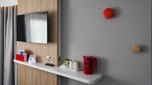Habitación de hotel moderna con televisor montado, estante blanco con diversos objetos y pared gris con detalles de madera.