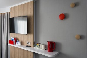 Habitación de hotel moderna con televisor montado, estante blanco con diversos objetos y pared gris con detalles de madera.