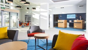 A modern hotel lobby with seating areas, a reception desk, and a large screen displaying the hotel name. - Holiday Inn Express Portsmouth - North by IHG (Portsmouth)