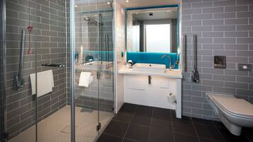 Un baño moderno con ducha envuelta en vidrio, un lavamanos blanco con detalles azules y un inodoro blanco.