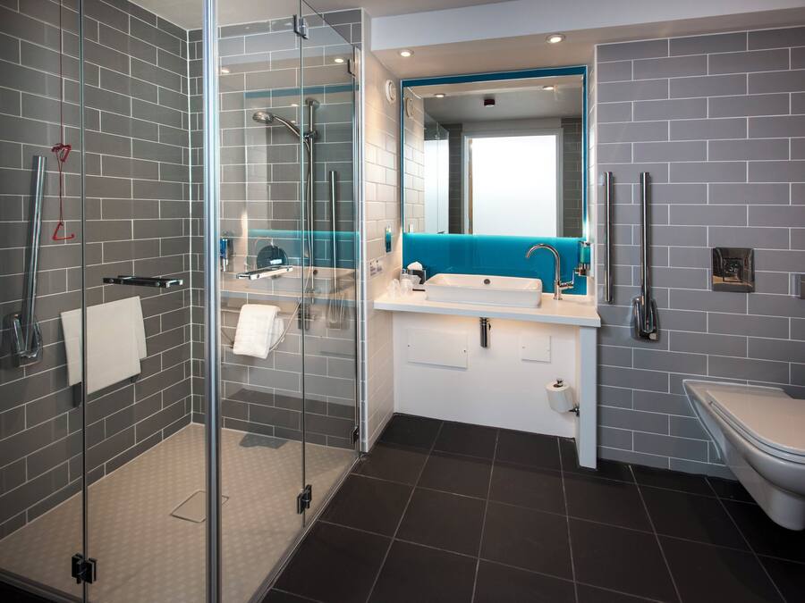 Un baño moderno con ducha envuelta en vidrio, un lavamanos blanco con detalles azules y un inodoro blanco.