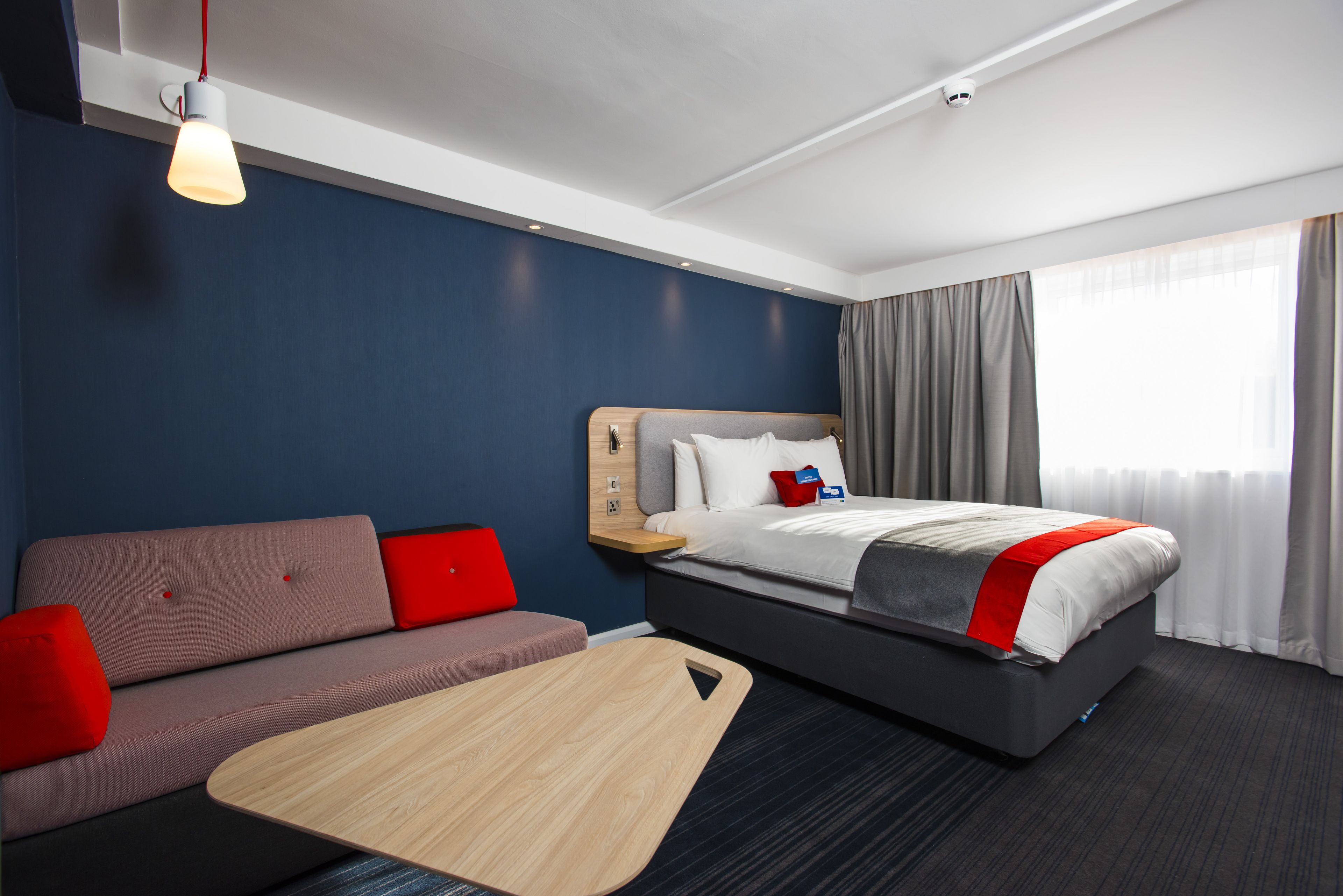 Quarto de hotel moderno com cama, sofá e uma pequena mesa de madeira.