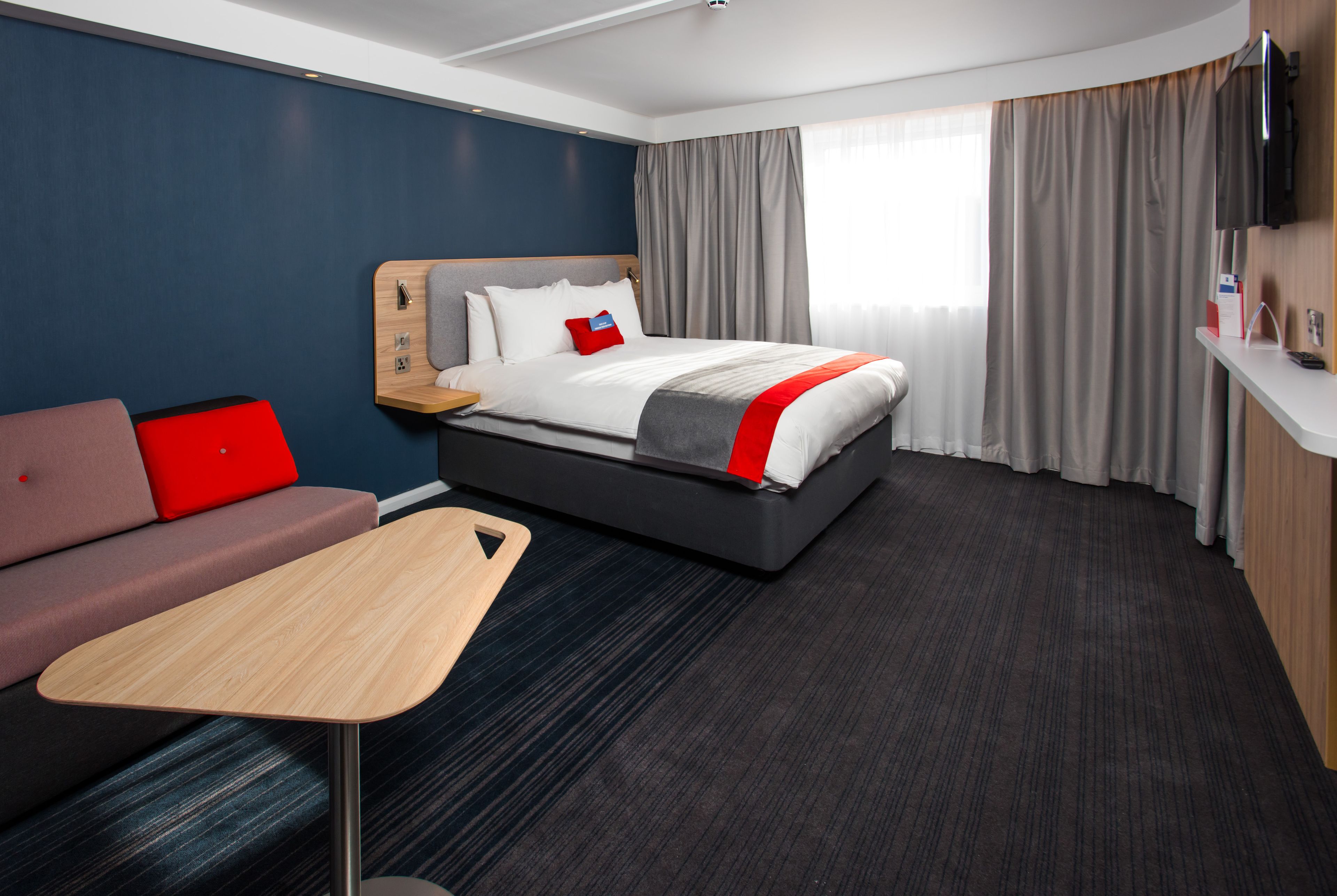 Una habitación de hotel con cama, escritorio, sofá y televisión.