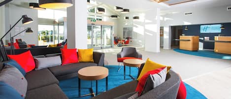 A modern hotel lobby with a large sectional sofa, a round coffee table, and a reception desk.