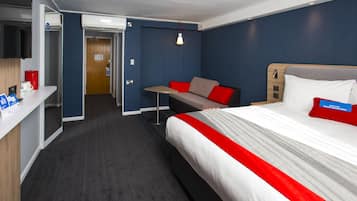 Quarto de hotel com uma cama, escrivaninha, cadeira e mesa pequena.