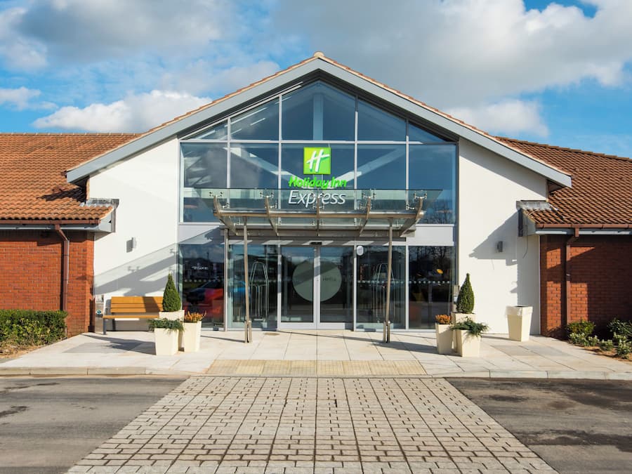 Een Holiday Inn Express hotel met een moderne glazen gevel, een bakstenen buitenkant en een heldere lucht.