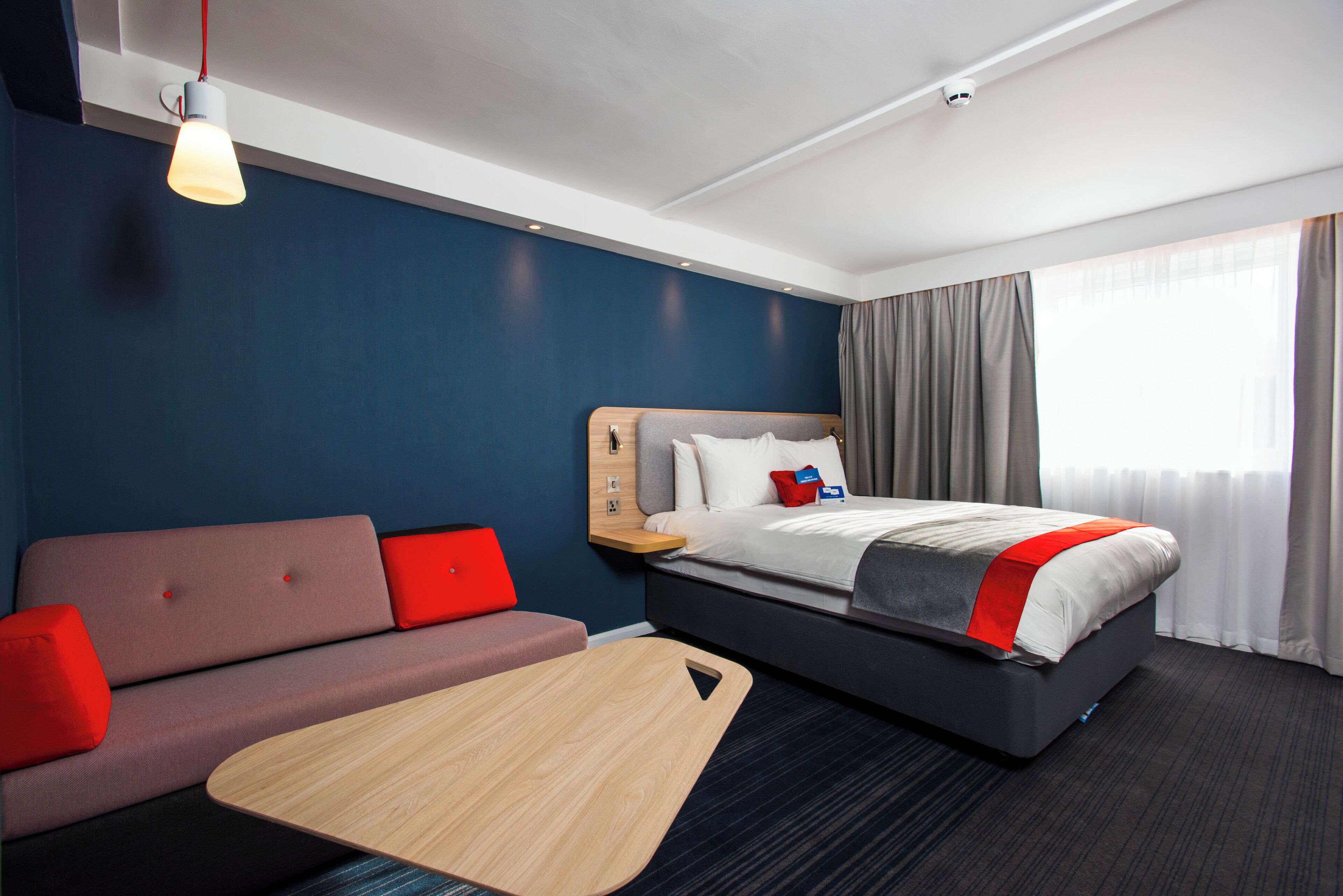 Une chambre d’hôtel avec un lit, un canapé, une petite table et une fenêtre avec des rideaux.