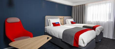 A hotel room with a bed, a desk, a chair, and a window with curtains.