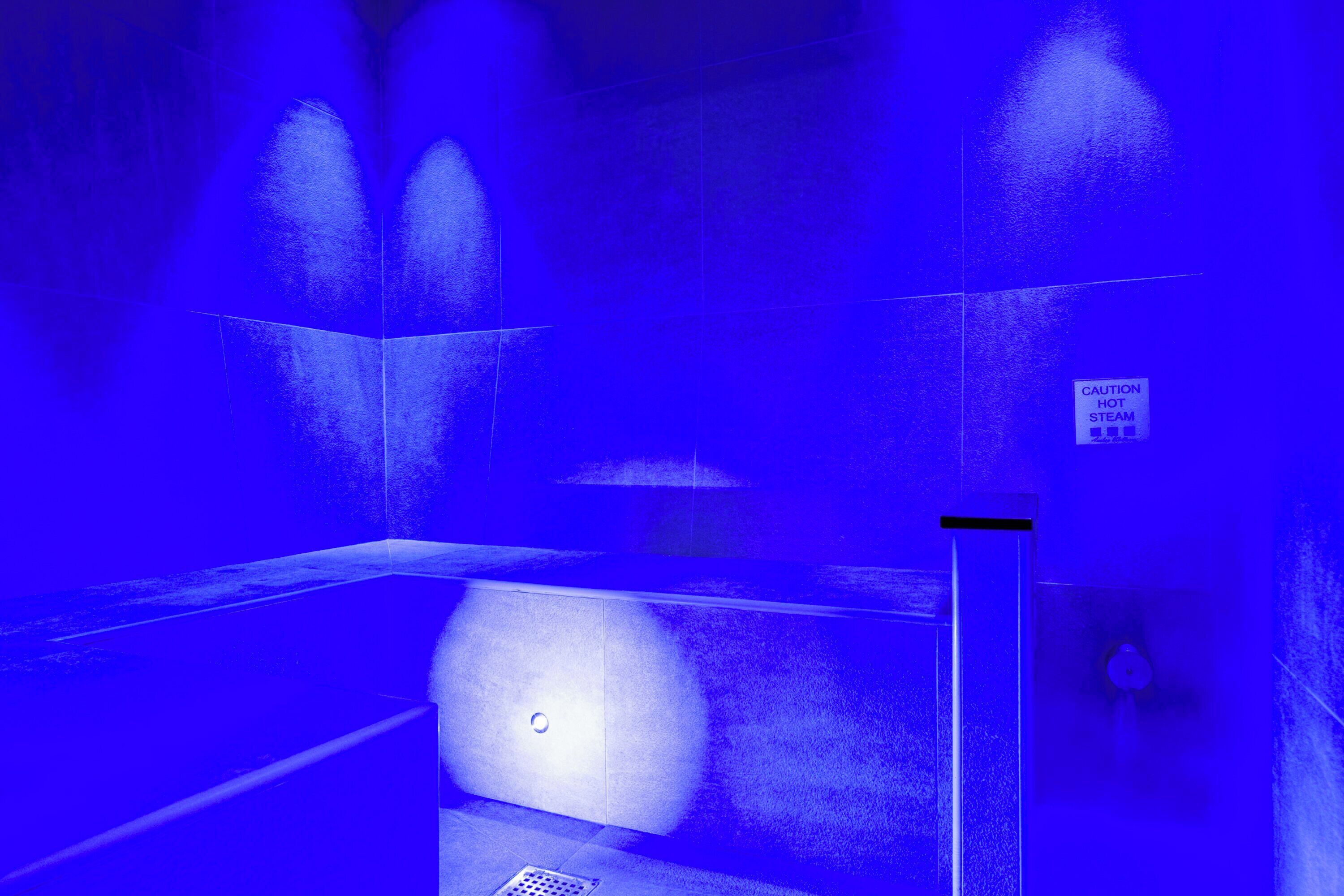 A blue-lit elevator interior with a caution sign for hot steam.