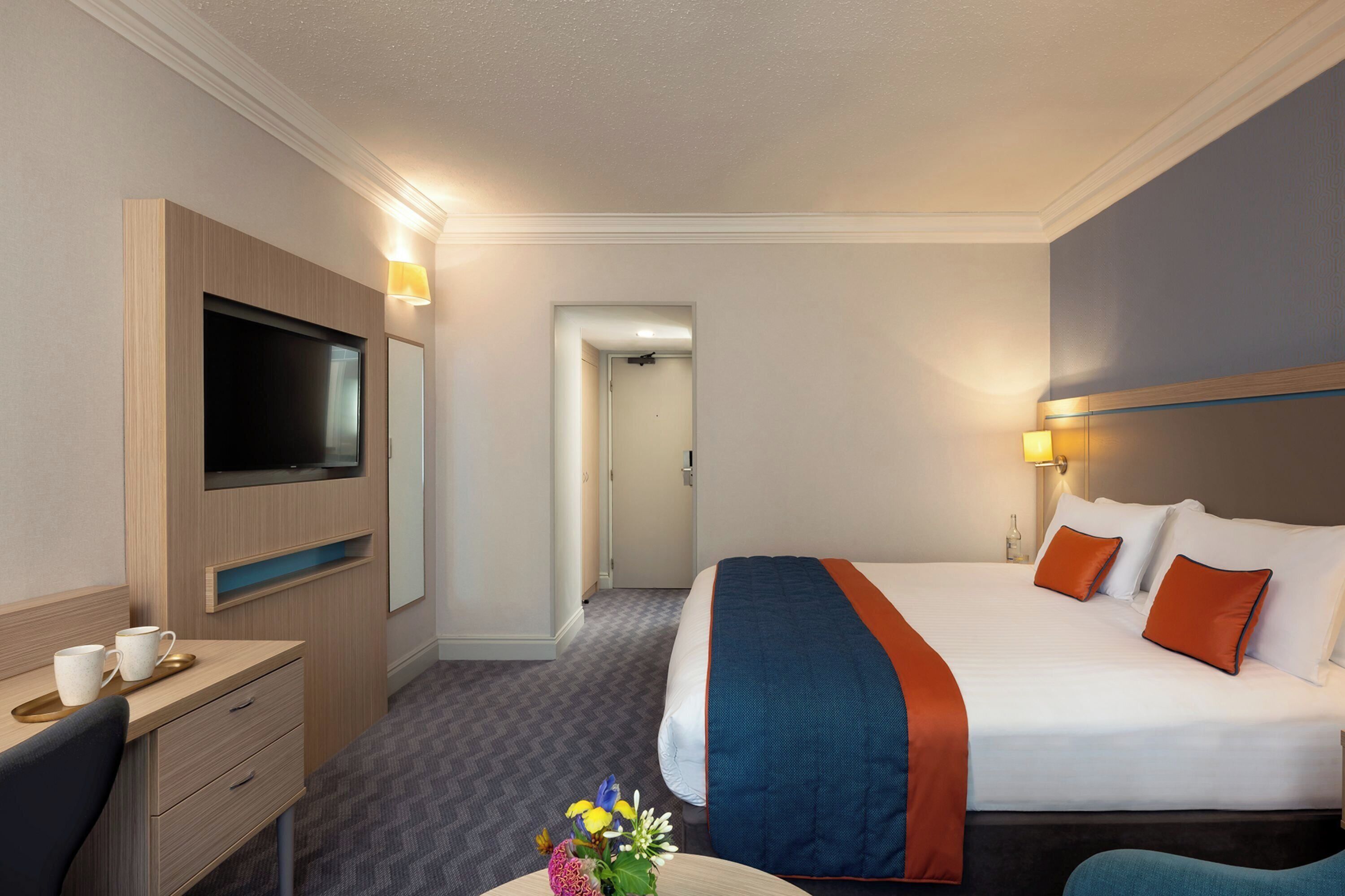 Ein Hotelzimmer mit einem Bett, einem Schreibtisch, einem Fernseher und einer Tür zu einem anderen Raum.