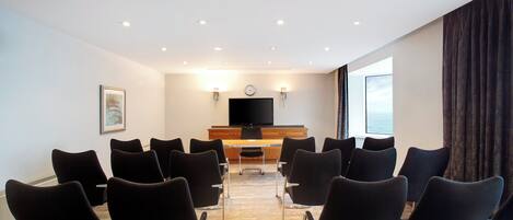 Une salle de conférence avec une longue table et de nombreuses chaises, un téléviseur à écran plat et une horloge au mur.