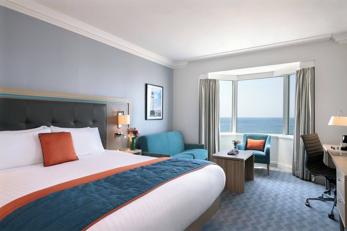 A hotel room with a large bed, a desk, a chair, and a view of the sea.