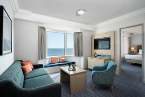 A hotel room with a sofa, a chair, a desk, a TV, and a view of the sea. - Leonardo Royal Hotel Brighton Waterfront  (Brighton)
