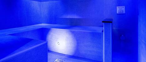 Sauna iluminada en azul con un cartel de precaución por el vapor intenso.