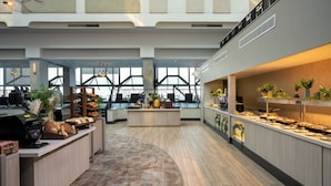 A spacious, modern hotel lobby with high ceilings, large windows, and a central island with food and beverages.