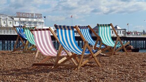 Beach chairs with striped fabric, a pier, and a building with 'BRIGHTON PIER' signage.