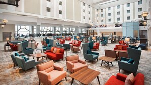 A spacious lobby with multiple seating areas, a central staircase, and large windows providing natural light.
