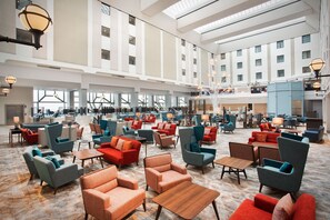 A spacious lobby with multiple seating areas, a central staircase, and large windows providing natural light.