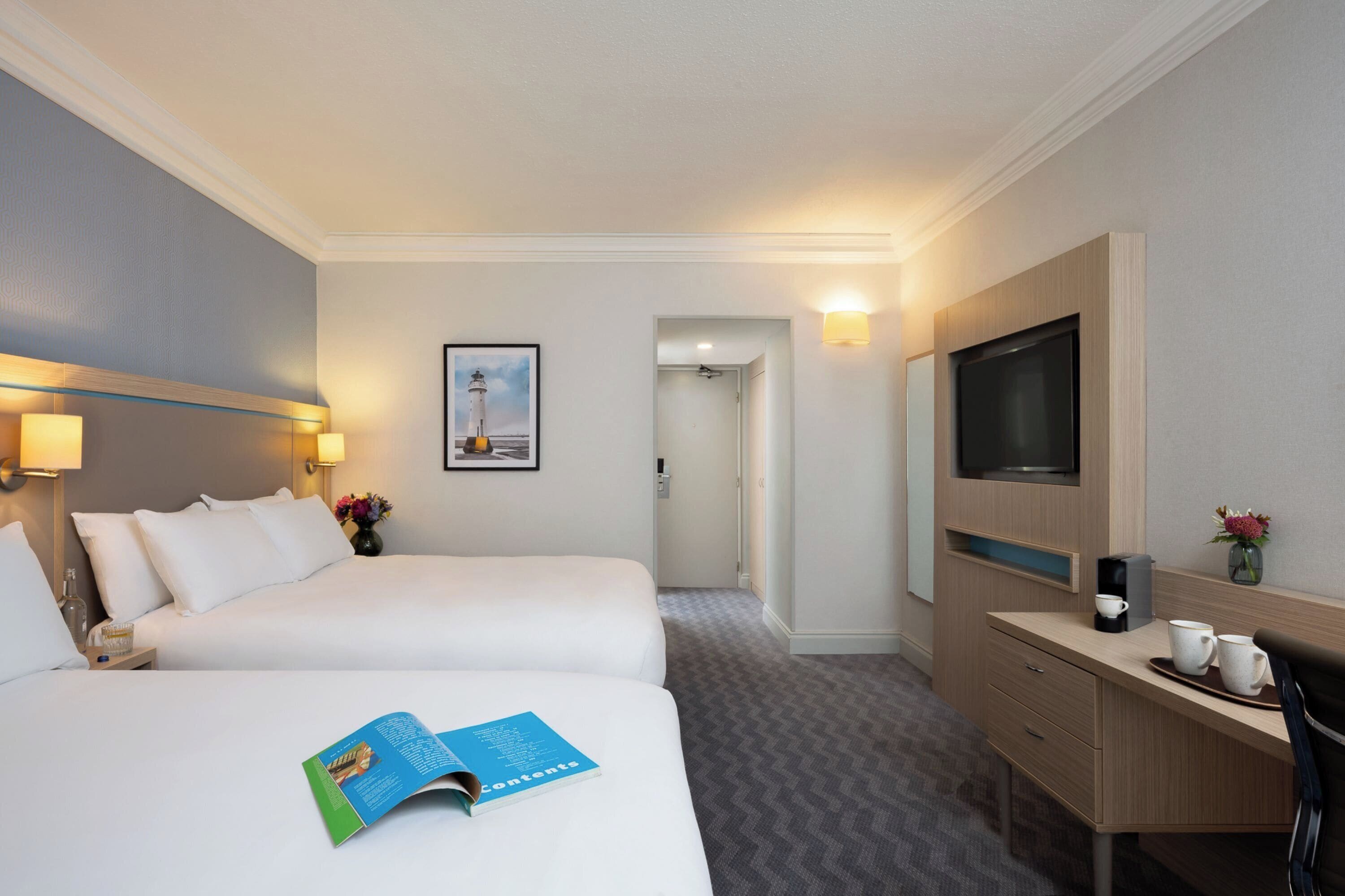 Une chambre d’hôtel avec deux lits, un bureau, une télévision et un tableau encadré au mur.