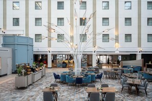A hotel lobby with a central decorative tree, multiple seating areas, and a buffet counter.