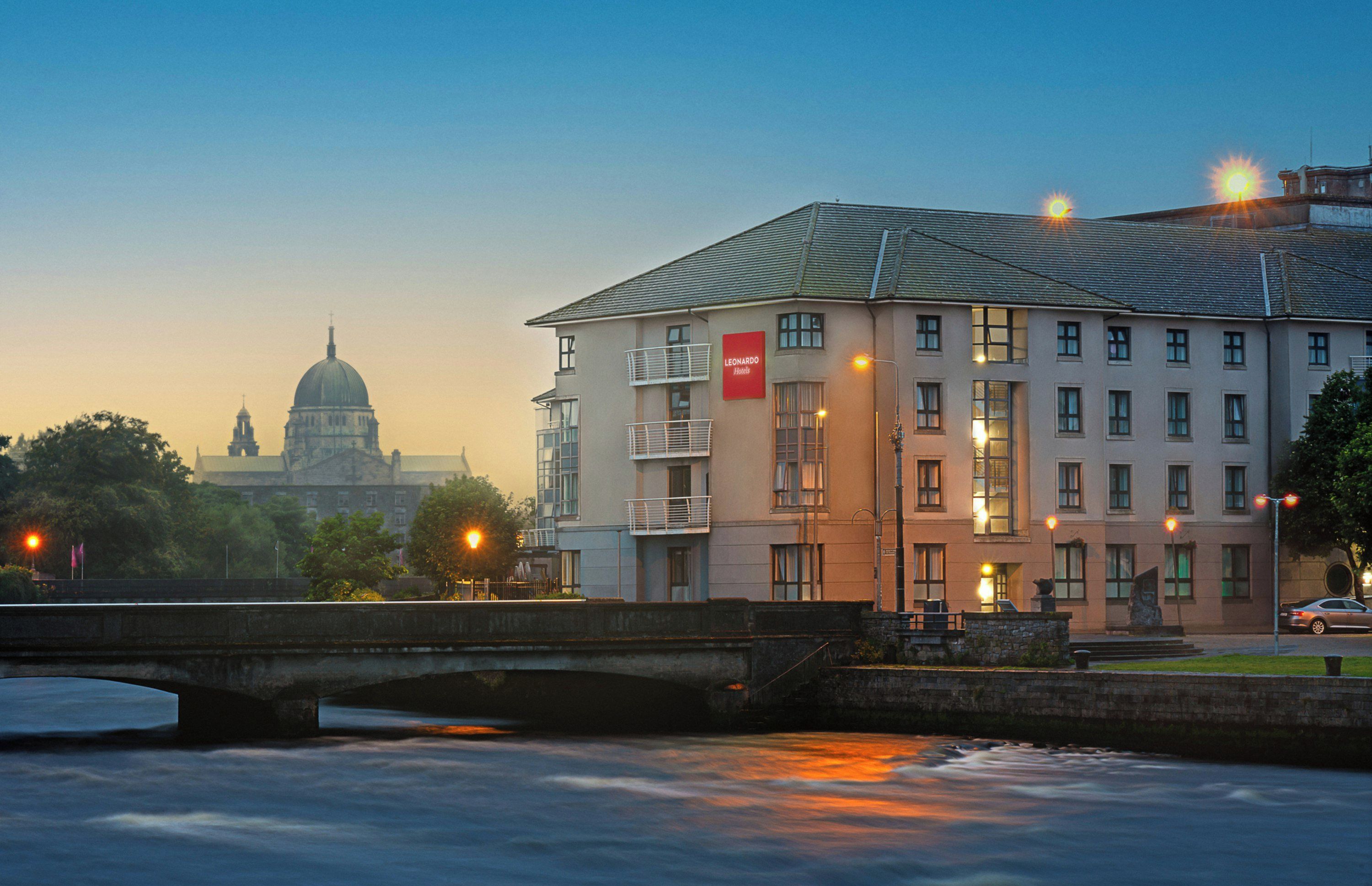 Un hotel con un letrero rojo, un puente y un río al frente.