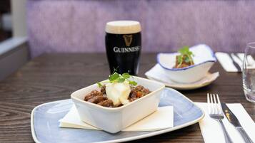 A bowl of stew with a garnish on a plate, a glass of Guinness beer, and a bowl of soup on a table.