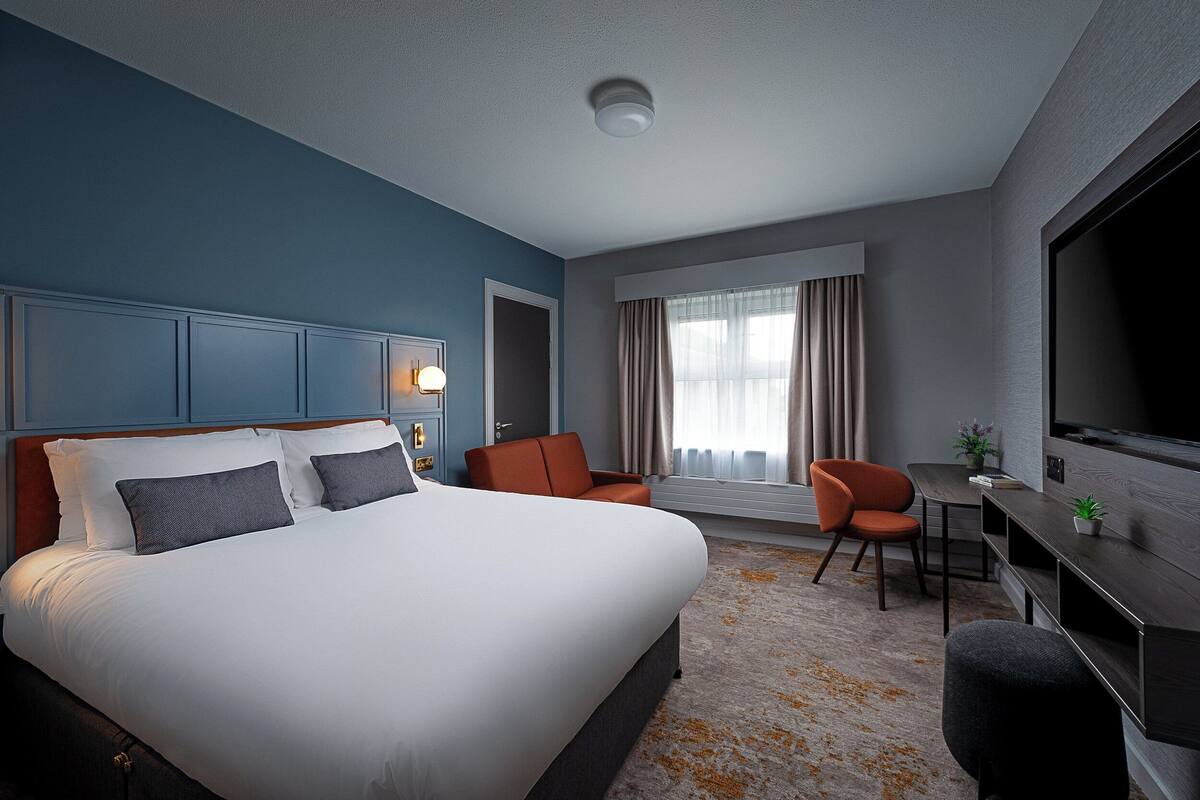 A hotel room with a large bed, a desk, a chair, a television, and a window with curtains.