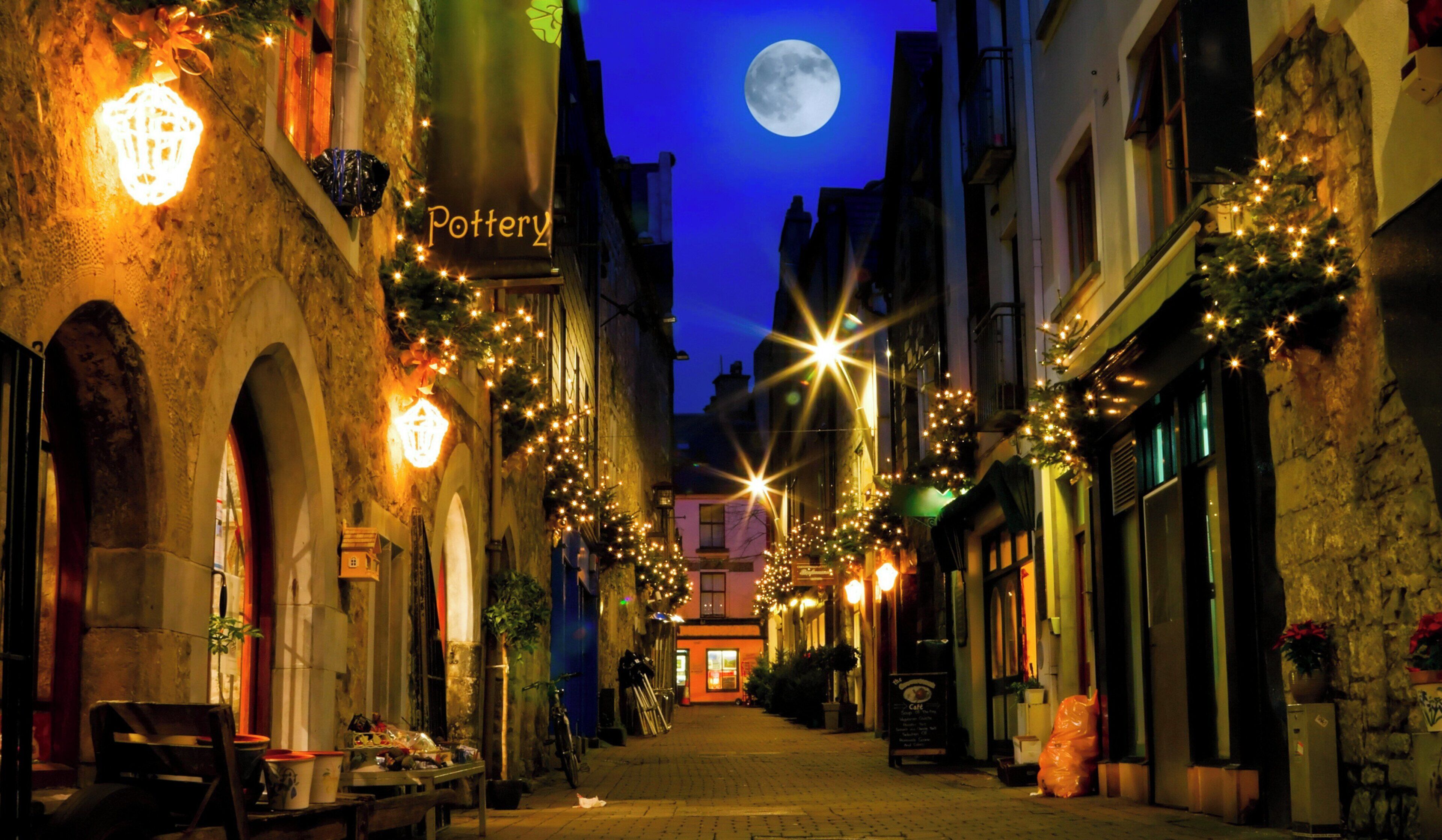 Una stretta via fiancheggiata da edifici, decorata con luci a stringa e un'insegna per una bottega di ceramiche.