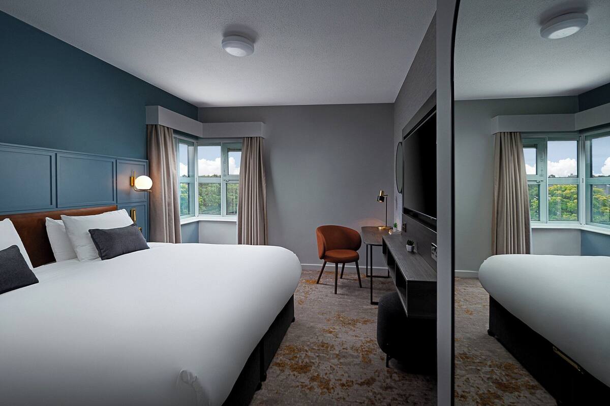 A hotel room with two beds, a desk, a chair, and a television.