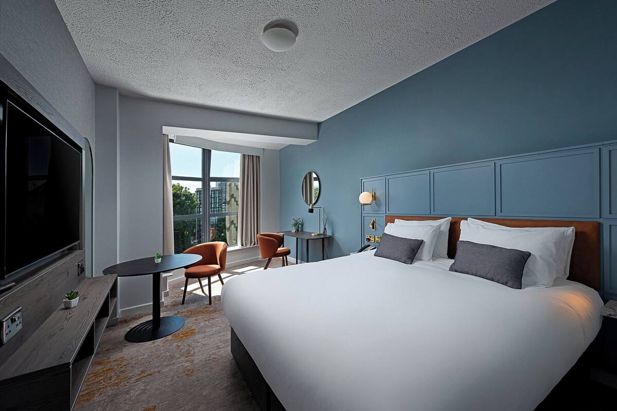 A hotel room with a large bed, a desk with a chair, a TV, and a window with curtains.