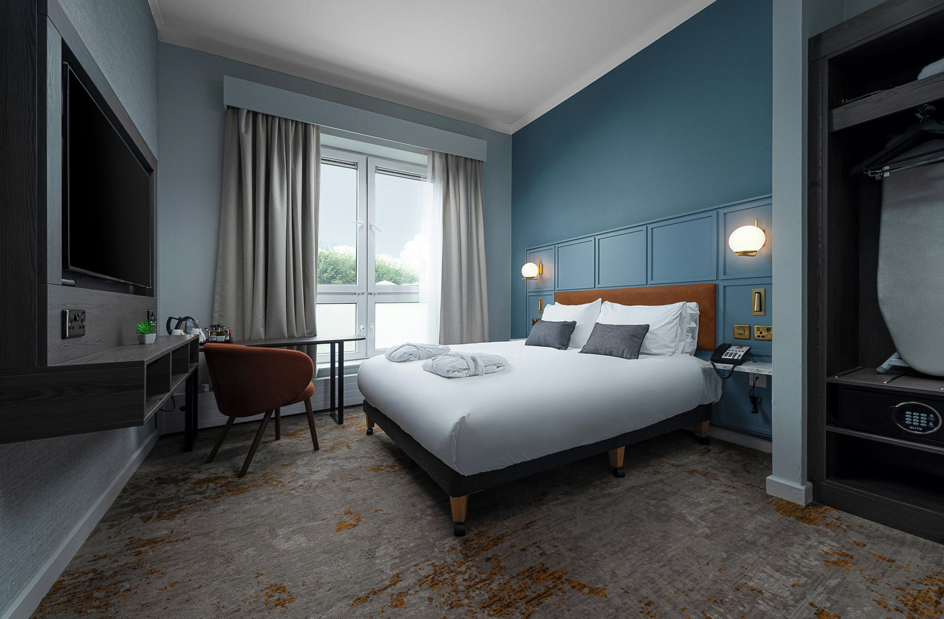 A hotel room with a bed, a desk, a chair, a wardrobe, and a window with curtains.