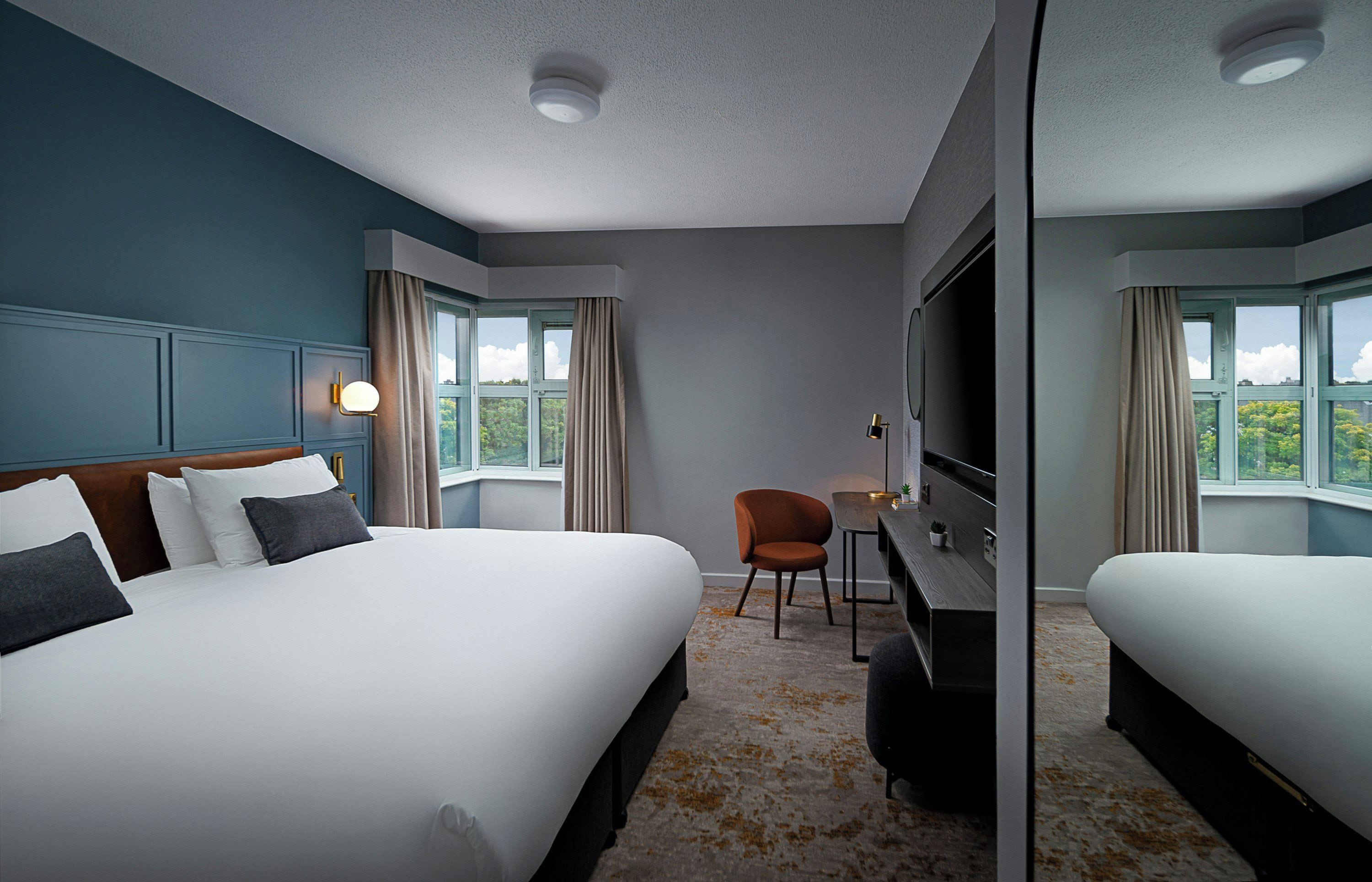 A hotel room with a large bed, a desk, a chair, and a TV.
