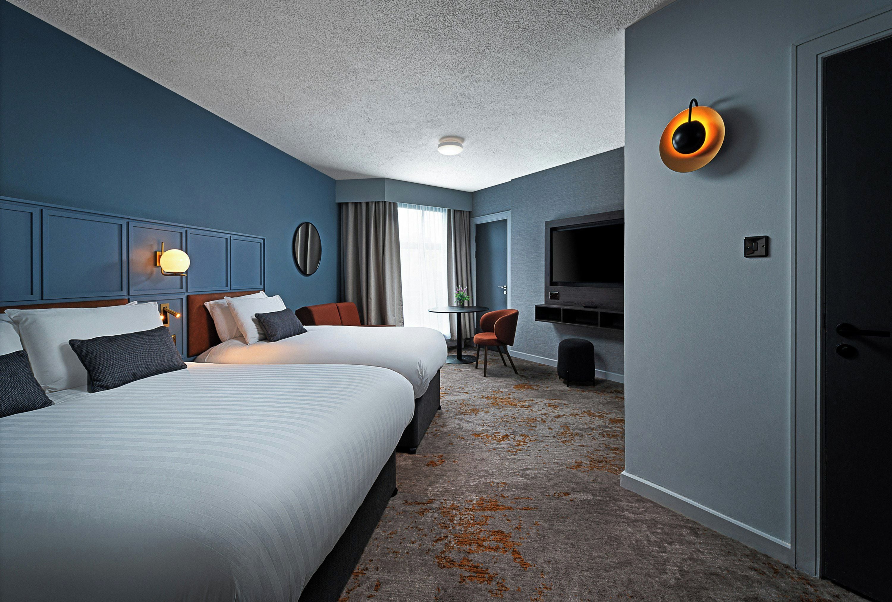 Une chambre d’hôtel avec deux lits, une télévision, un bureau et une chaise.