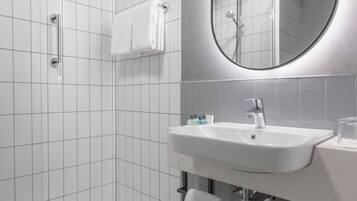 A modern bathroom with white tiles, a large mirror, a sink, and a shower area.